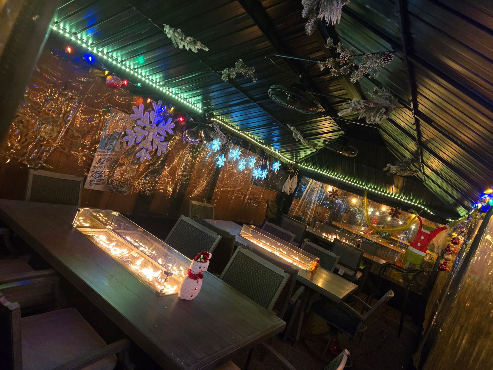 A festive outdoor dining area decorated with Christmas lights and snowflakes, with tables and chairs set up.