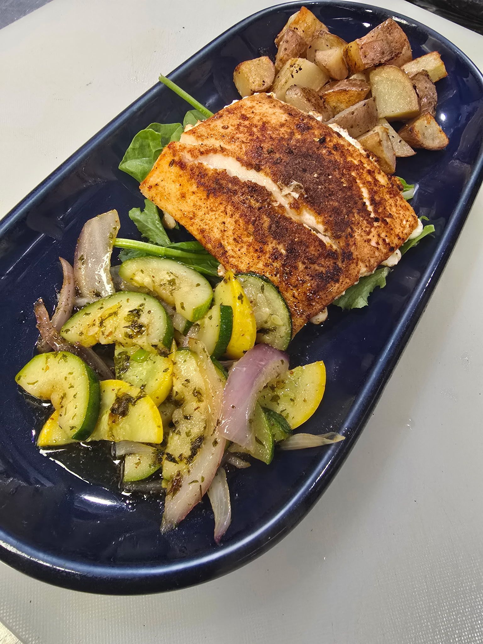 Grilled mahi mahi with red skin potatoes, mixed vegtables  and coleslaw on a blue platter.