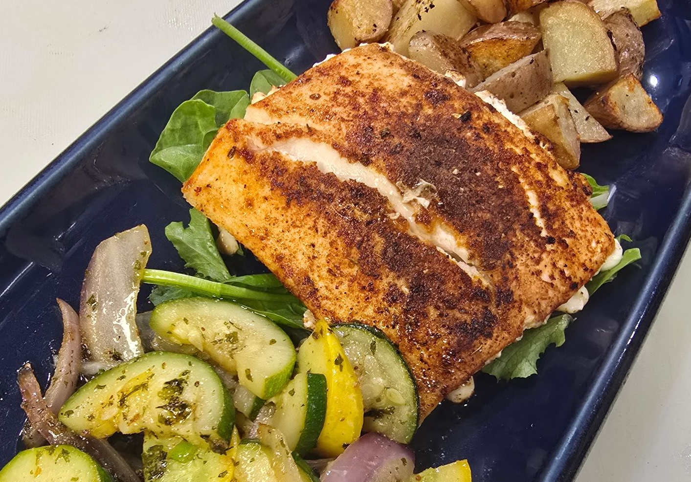 Grilled salmon fillet with vegetables and potatoes on a blue plate.