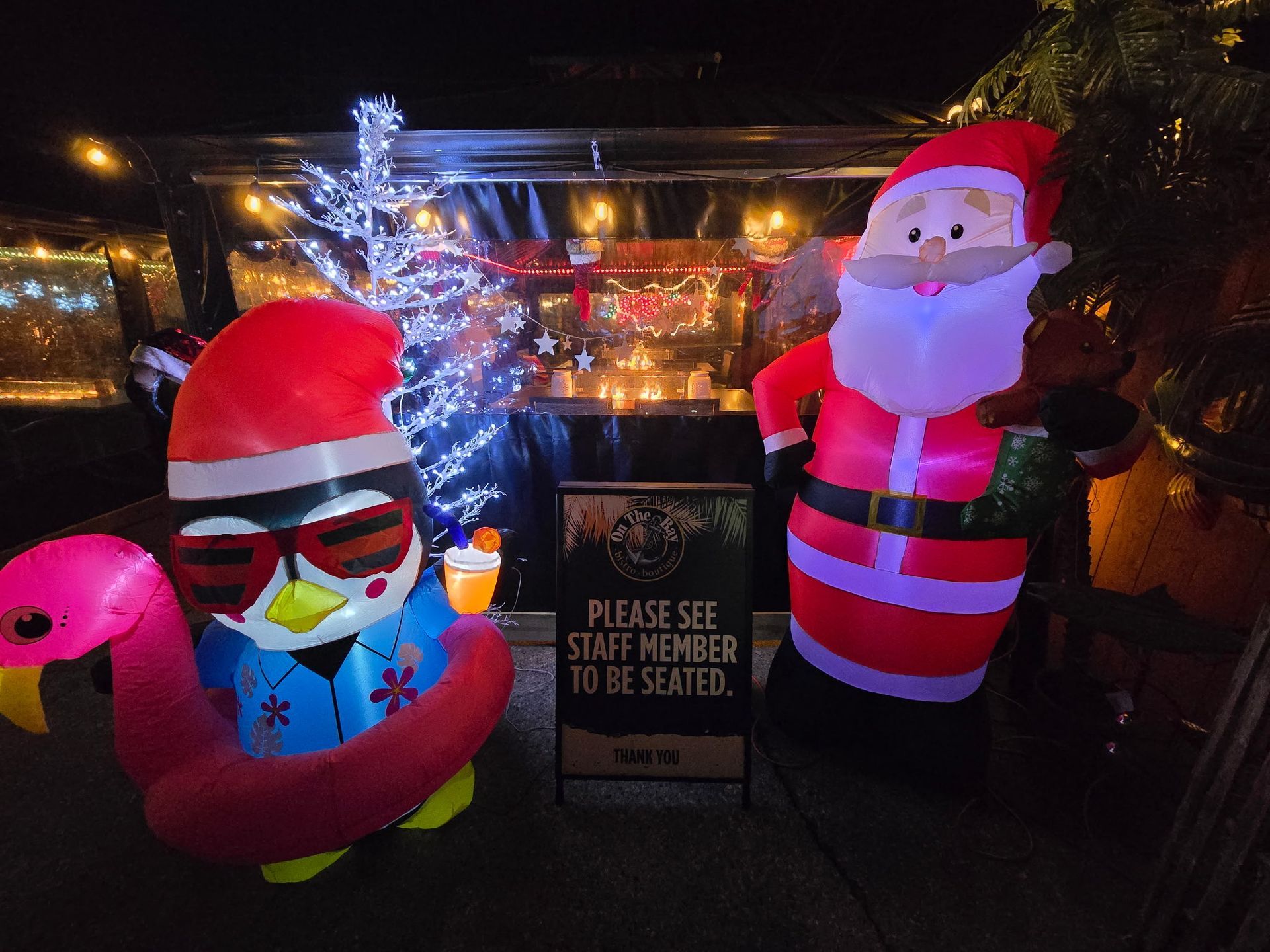 Inflatable Santa and penguin with flamingo float at an outdoor bar, lit up at night.