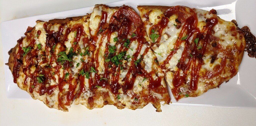 Pizza topped with cheese, sauce, and herbs, on a white rectangular plate.