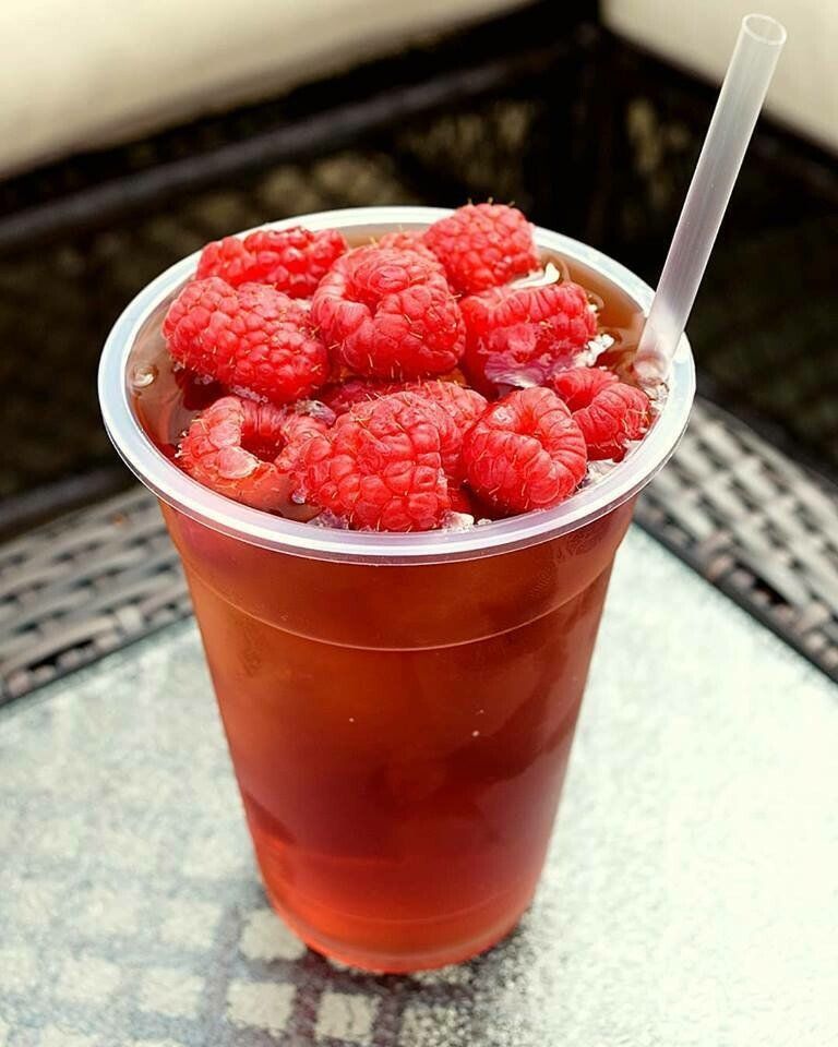 Iced raspberry tea in clear plastic cup, topped with fresh red raspberries, straw.