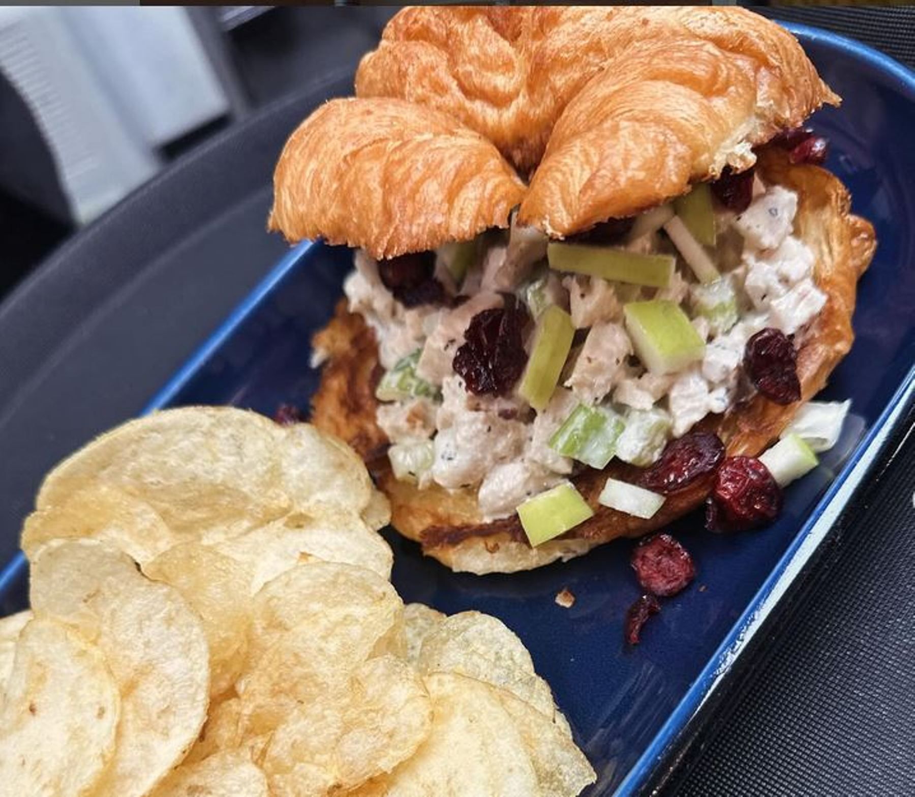 Chicken salad sandwich on a croissant with chips on a blue plate.