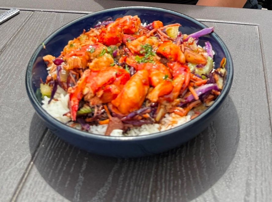 Lobster bowl with rice, red cabbage, carrots, and sauce in a blue bowl on a wood table.