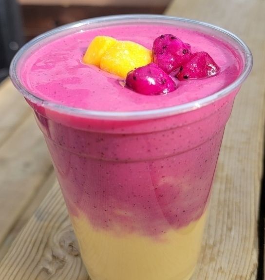 A close up of a pink smoothie in a plastic cup.