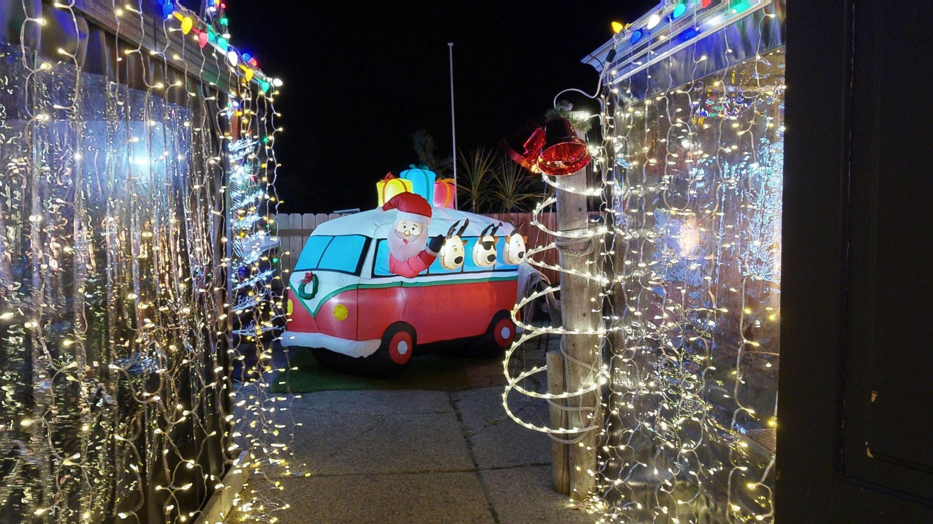 Christmas pop up with lights leading to a red VW bus with penguins and gifts; nighttime holiday setting.
