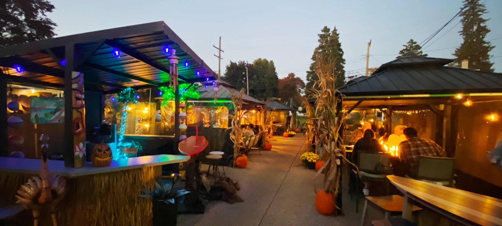 Outdoor bar with illuminated huts, pumpkins, and patrons.