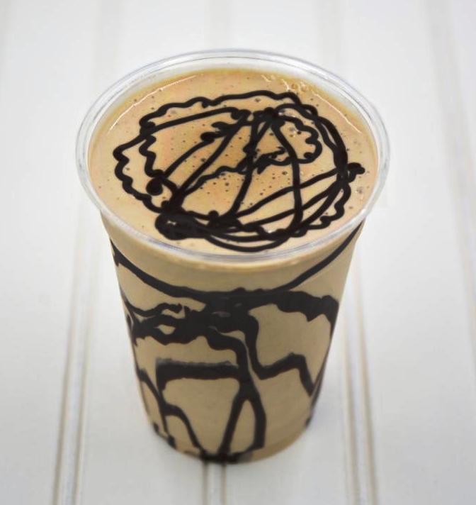Coffee milkshake in a clear cup, drizzled with chocolate on a white surface.