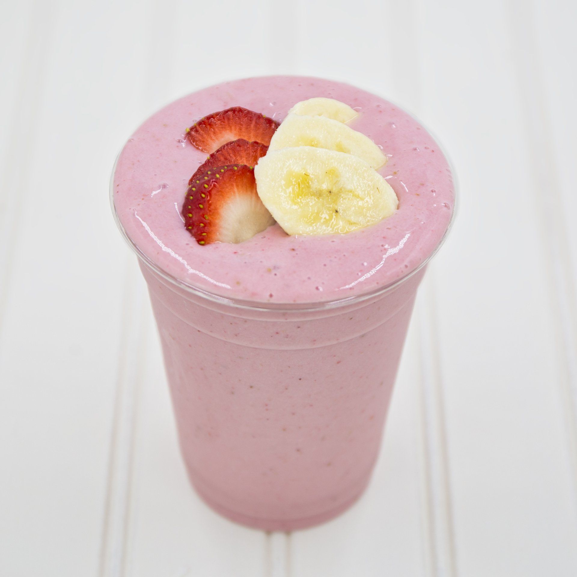 Strawberry banana smoothie in a clear cup, garnished with strawberry slices and banana.