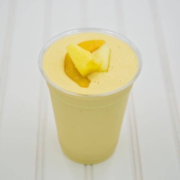 Yellow smoothie in a clear plastic cup, garnished with pineapple chunks.