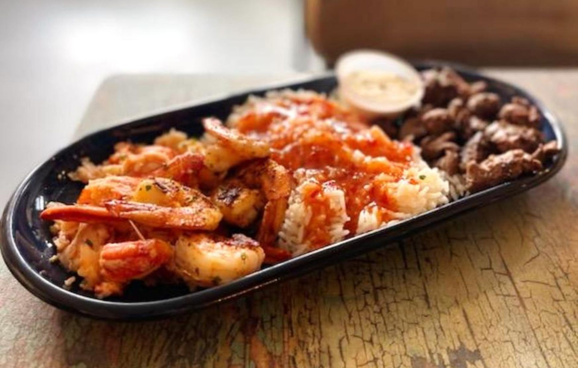 Plate with fried shrimp, rice, and steak, drizzled with red sauce.