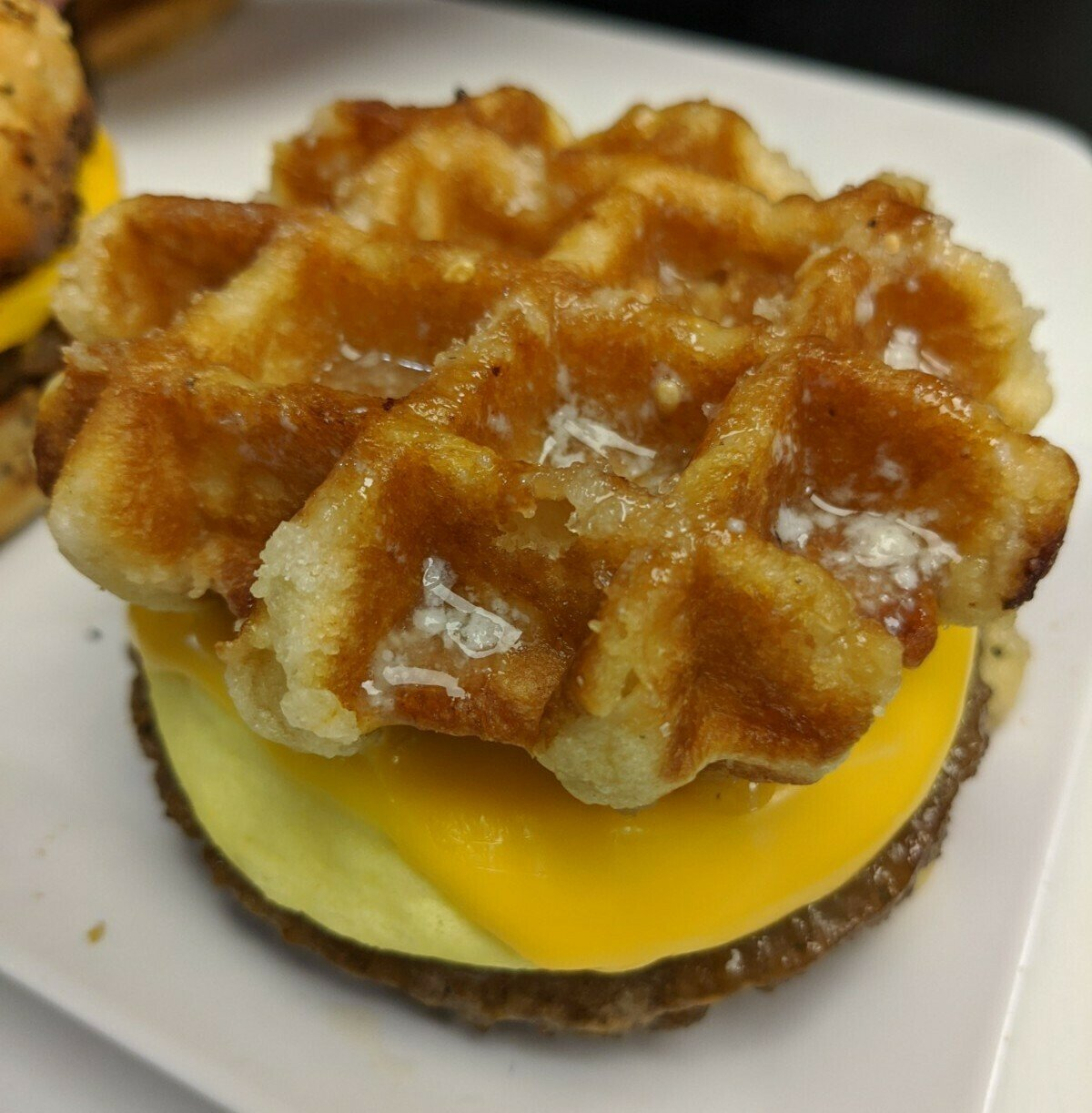 Waffle sandwich with egg, cheese, and sausage. Close-up shot, on a white plate.