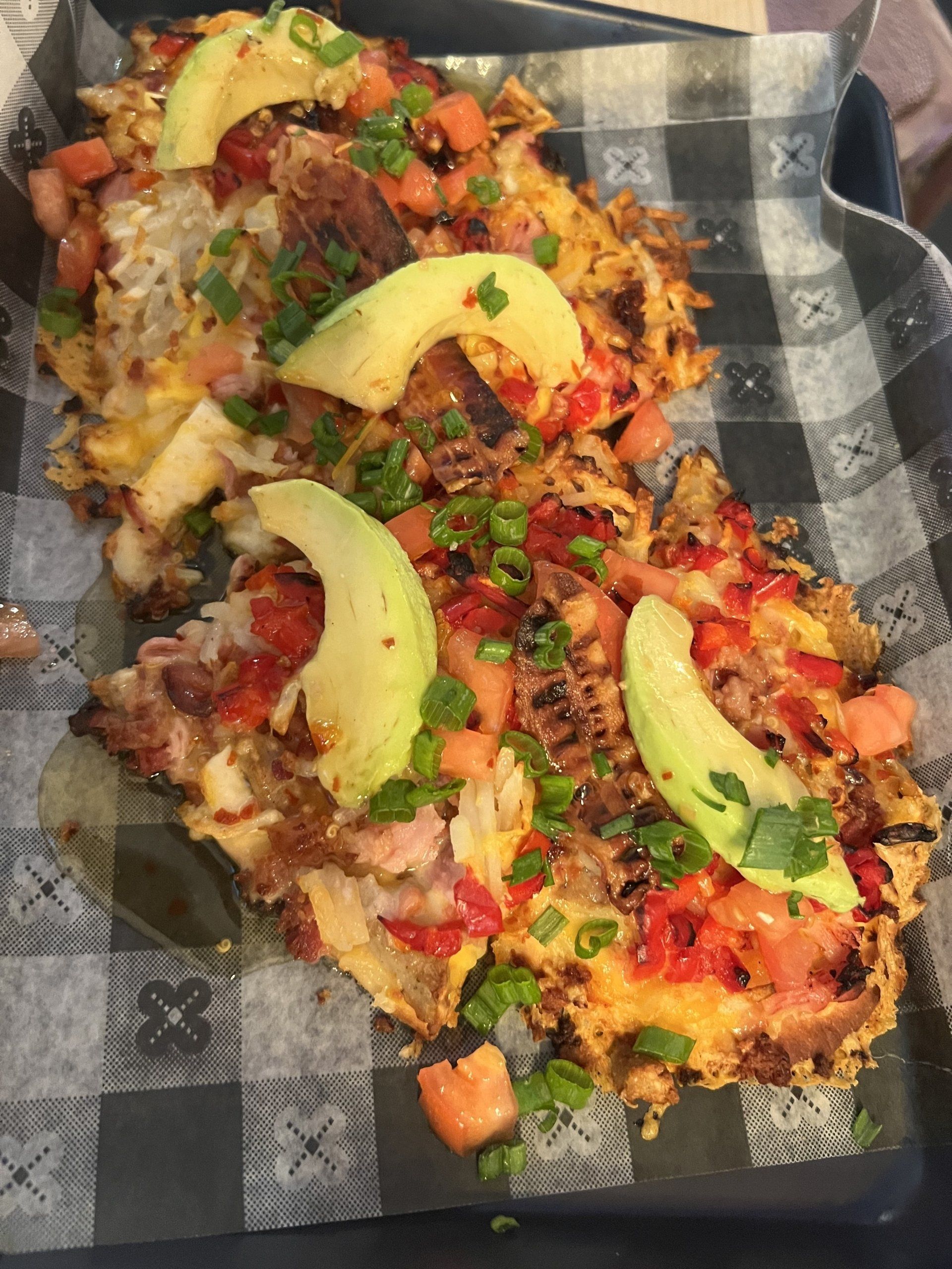 Potato cakes topped with avocado, diced tomatoes, and green onions on a checkered paper.