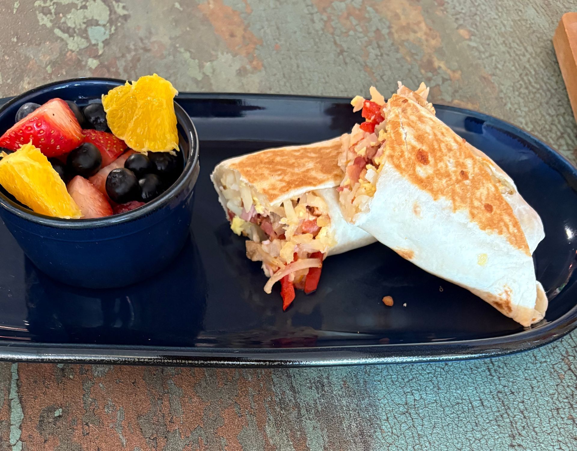 Breakfast burrito with fruit salad on a blue plate.