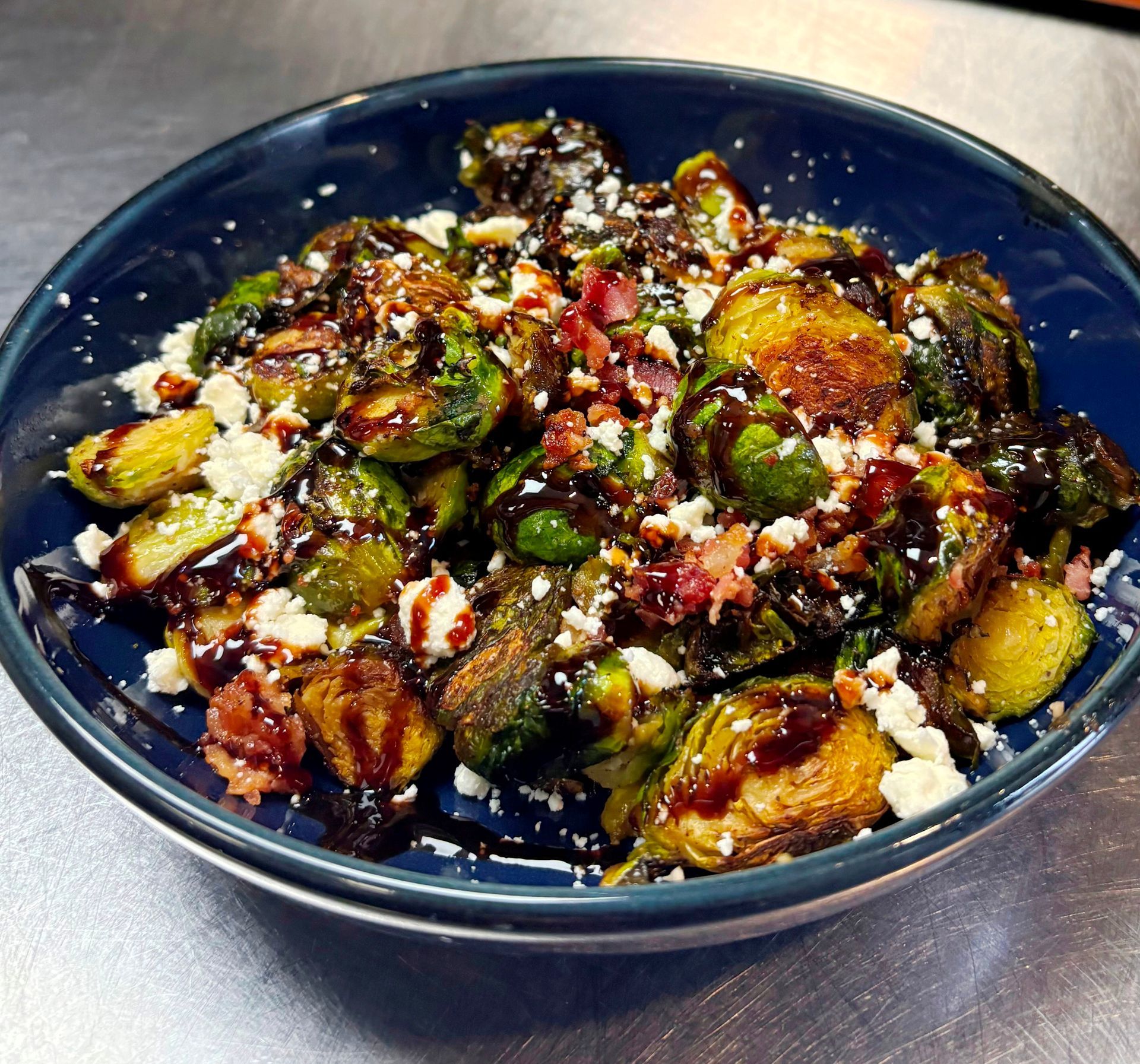 Roasted Brussels sprouts with bacon, balsamic glaze, and feta cheese in a blue bowl.