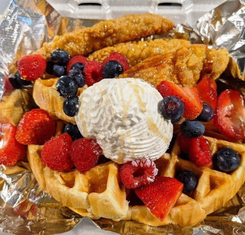 Chicken and waffles topped with berries and whipped cream.