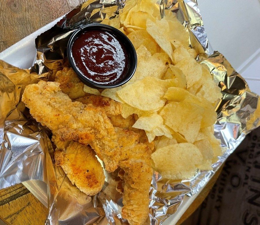 Fried chicken tenders, potato chips, and BBQ sauce in a takeout container.