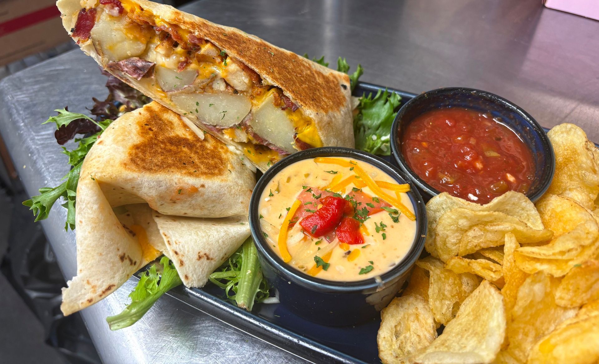 Breakfast burrito with salsa, cheese sauce, and chips on a plate.