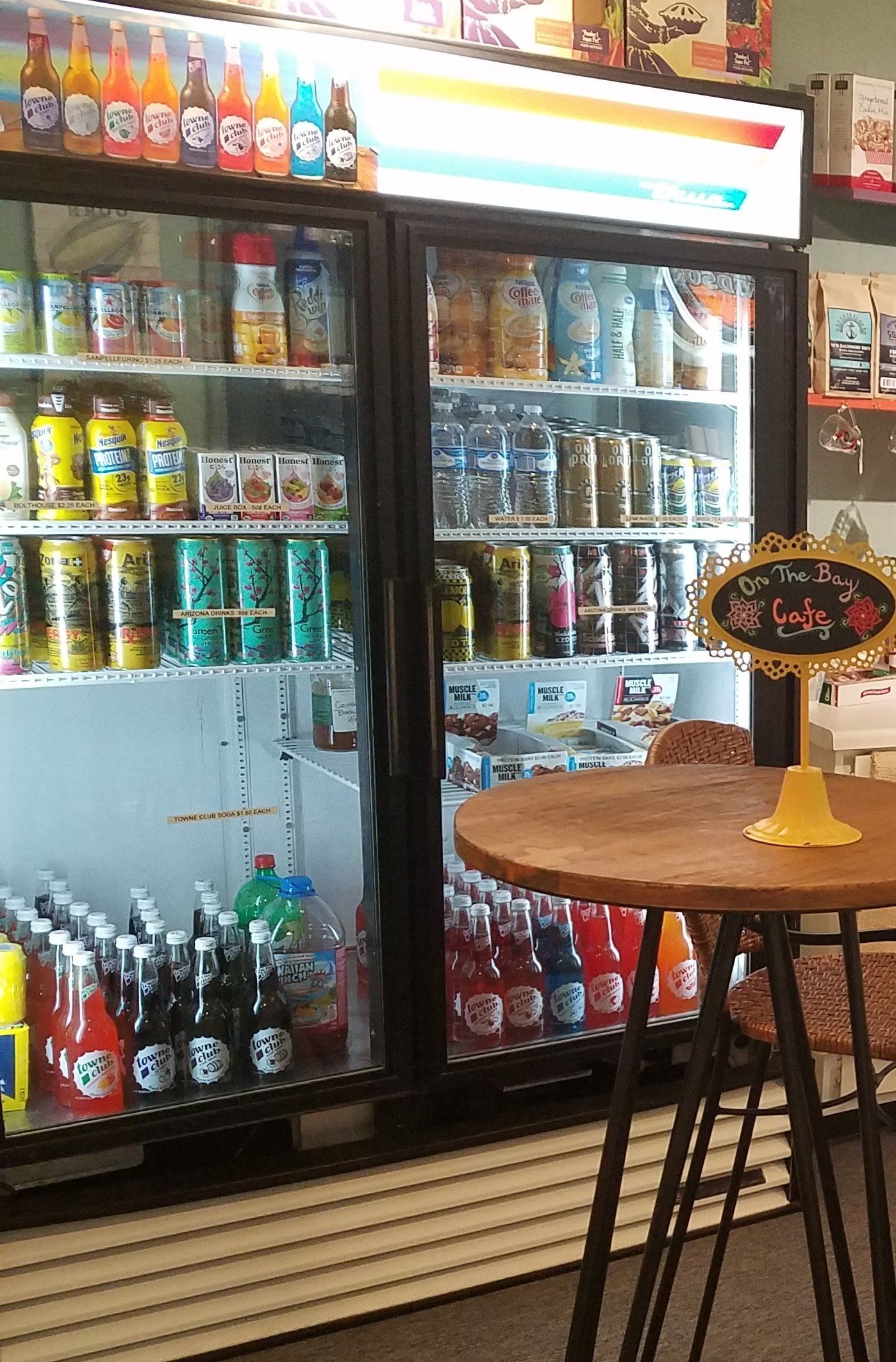 Refrigerated beverage display case inside a shop, filled with colorful drinks; a small table is in the foreground.