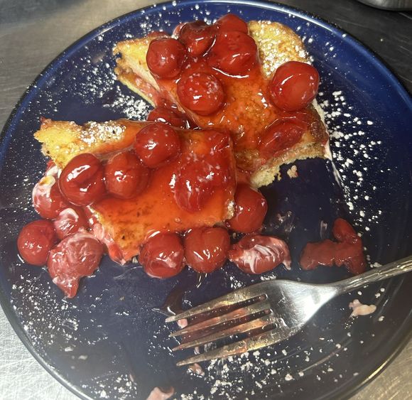 French toast with cherry sauce and powdered sugar on a blue plate. A fork rests on the plate.