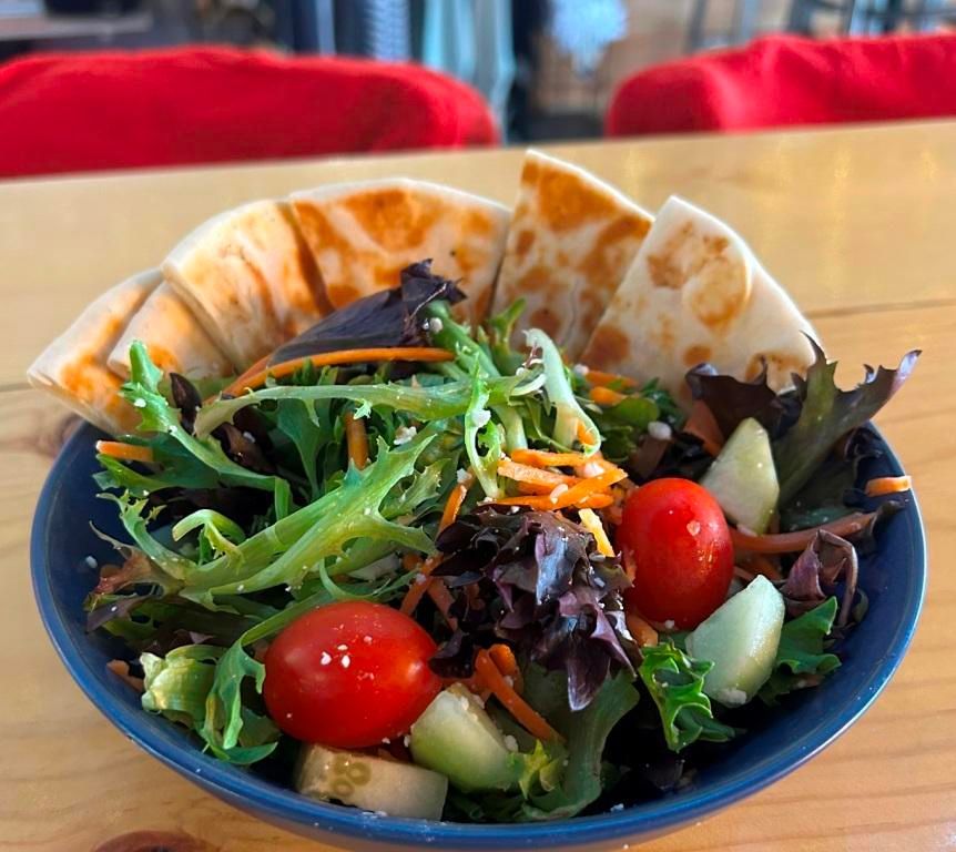 Salad with pita bread, cherry tomatoes, cucumbers, and carrots in a blue bowl on a wooden table.