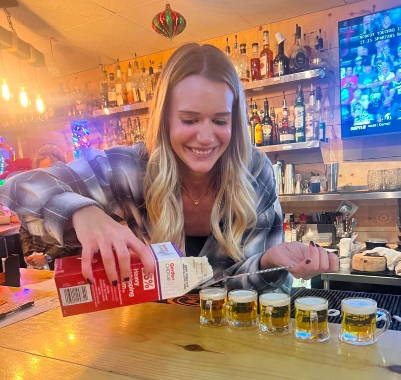 A woman is pouring milk into shot glasses at a bar.