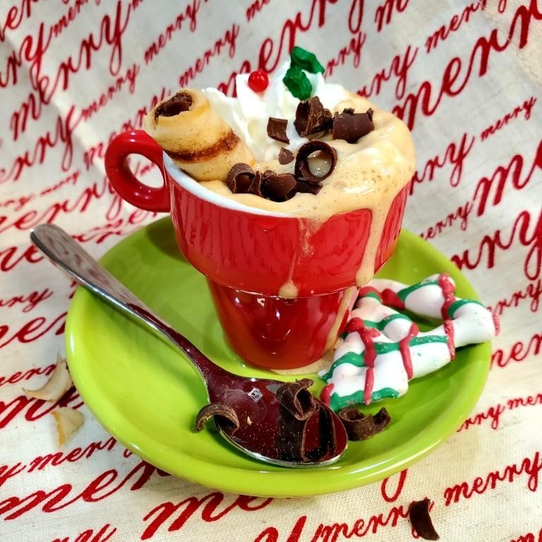 Red mug with whipped cream, chocolate curls, and a wafer roll on a green saucer with candy cane.