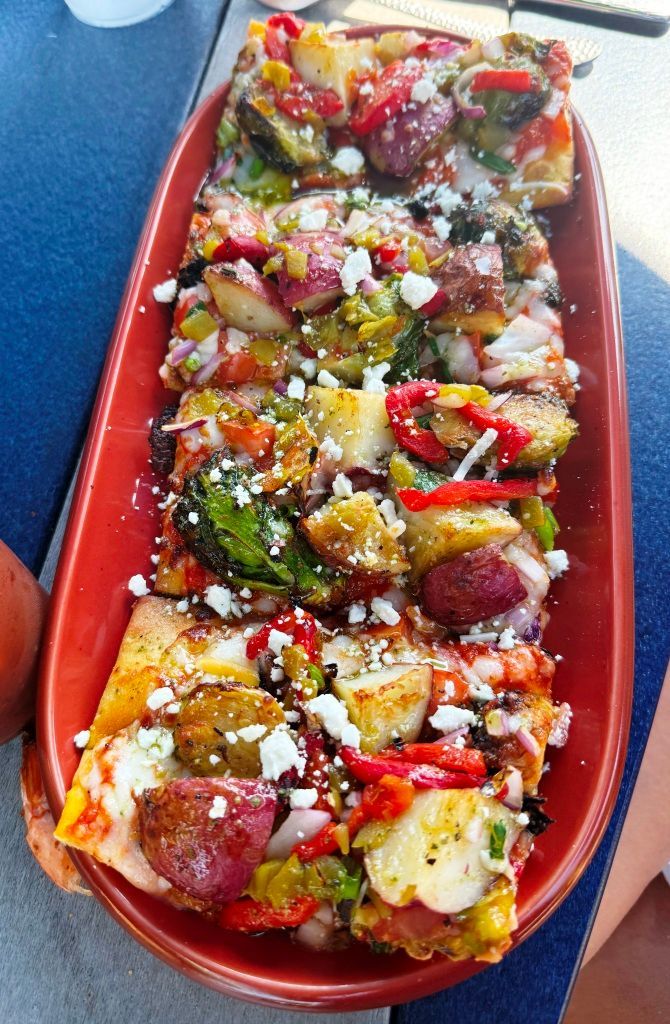 Rectangular pizza topped with roasted vegetables, sausage, and cheese on a red platter.