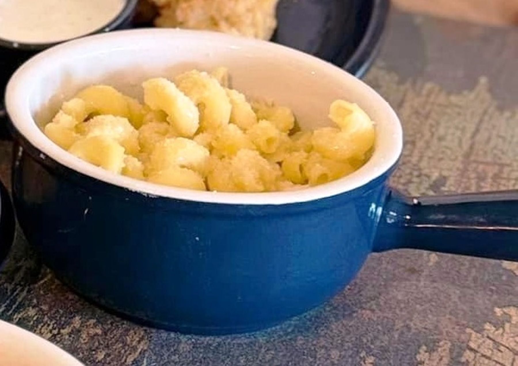 Macaroni and cheese in a small blue bowl with a handle, on a table.