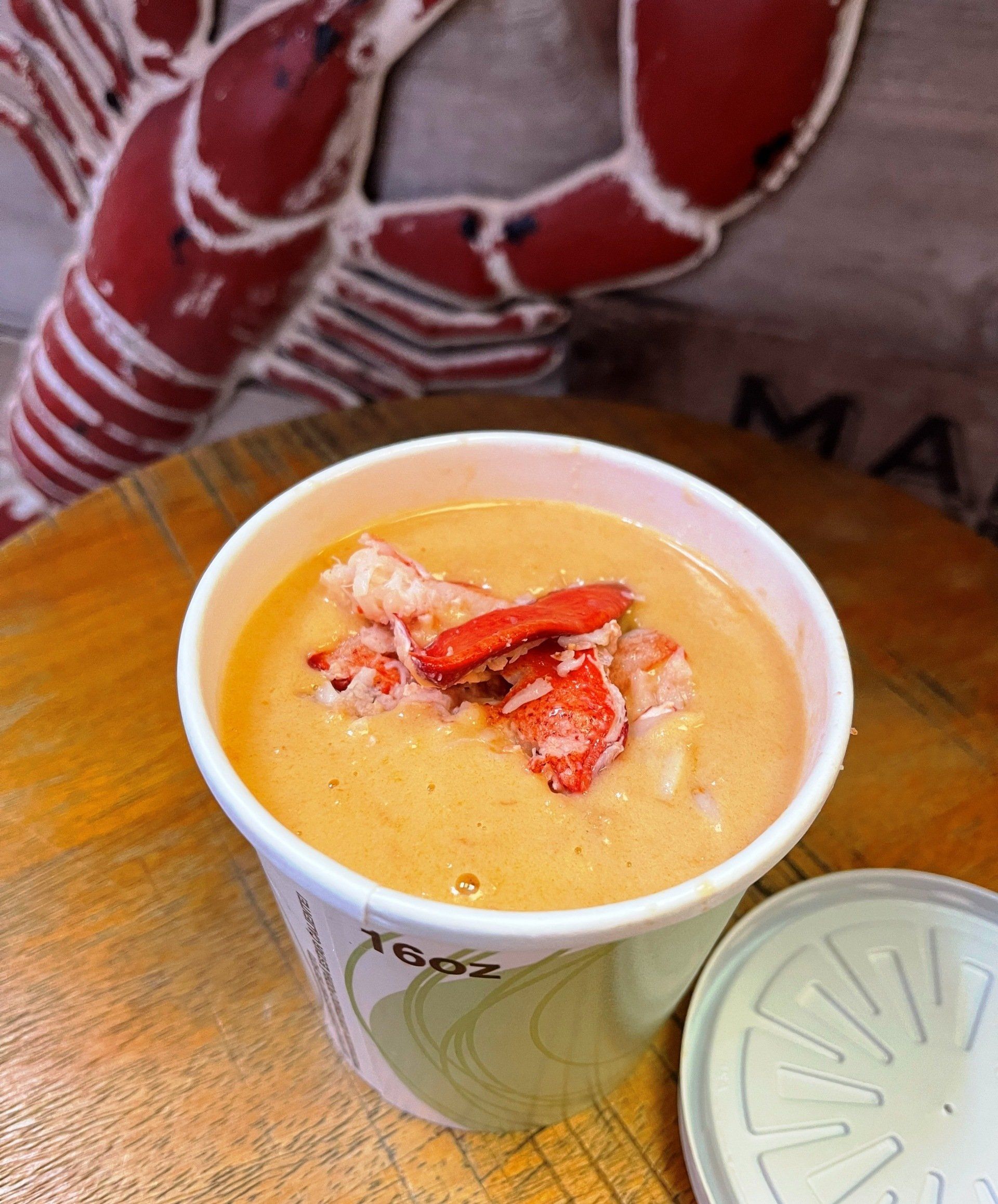 A cup of soup with a lobster on top of it