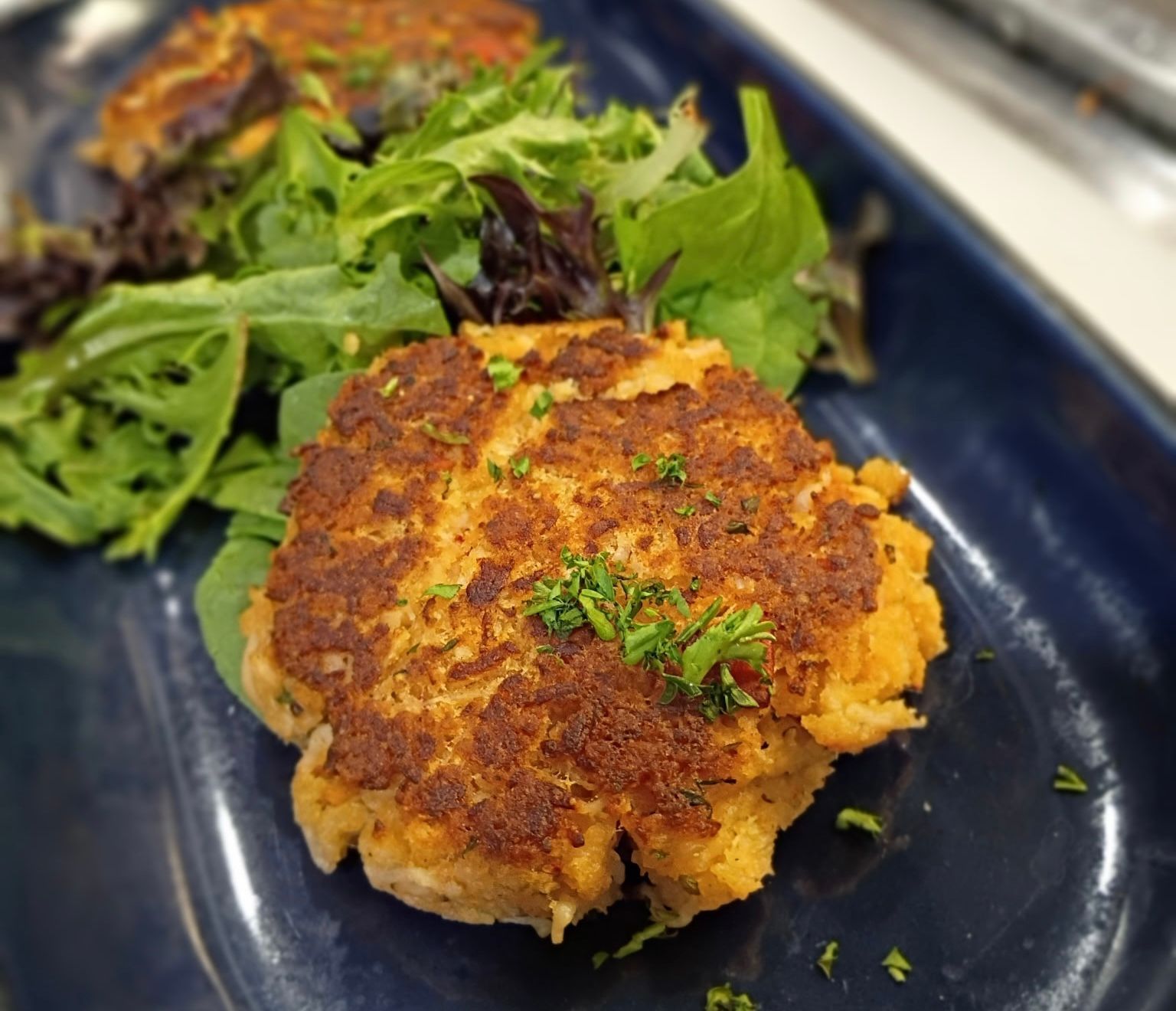 Crab cakes with green salad on a blue plate.