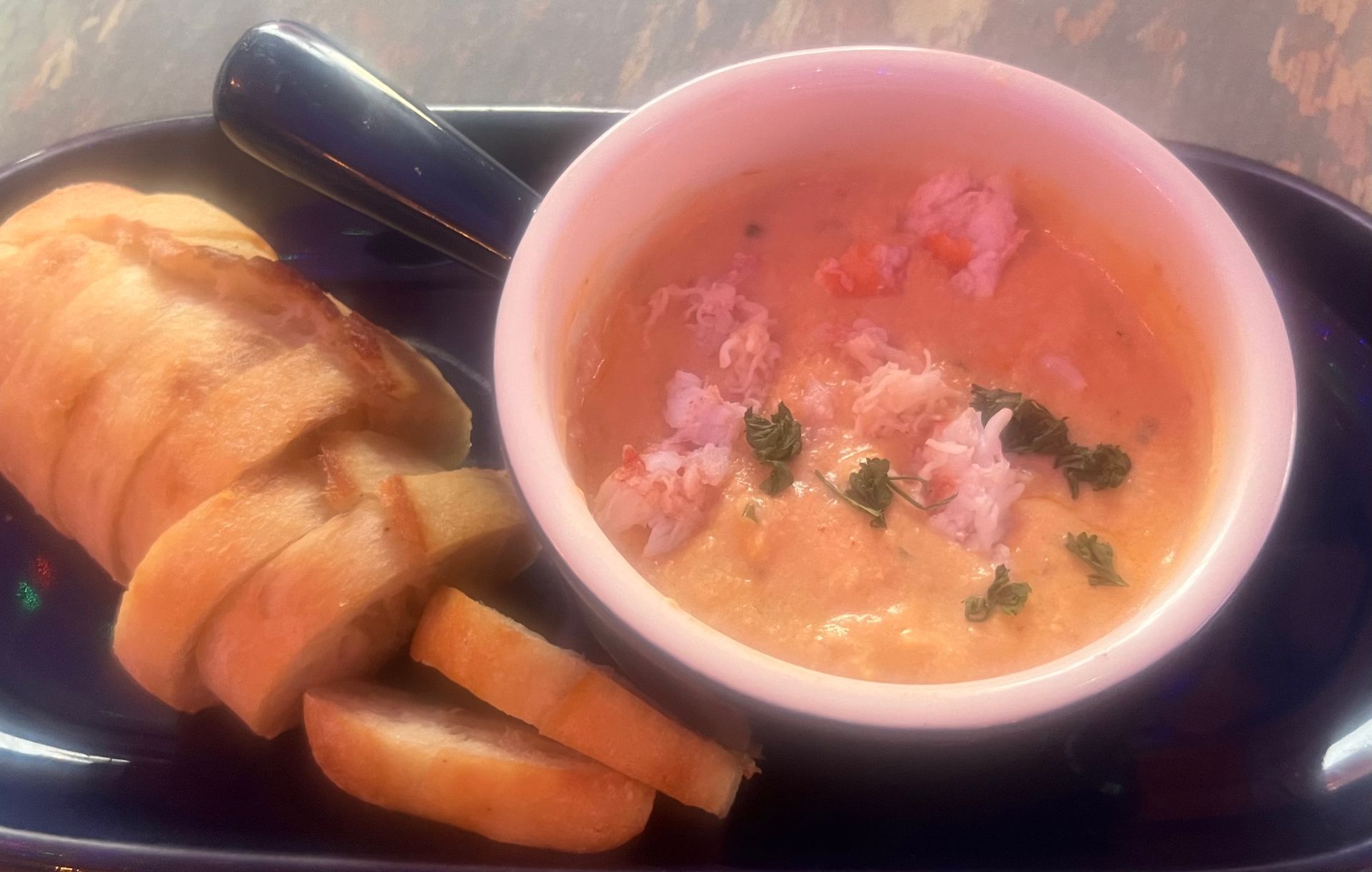 Crab bisque in a white bowl, bread slices alongside on a blue plate.