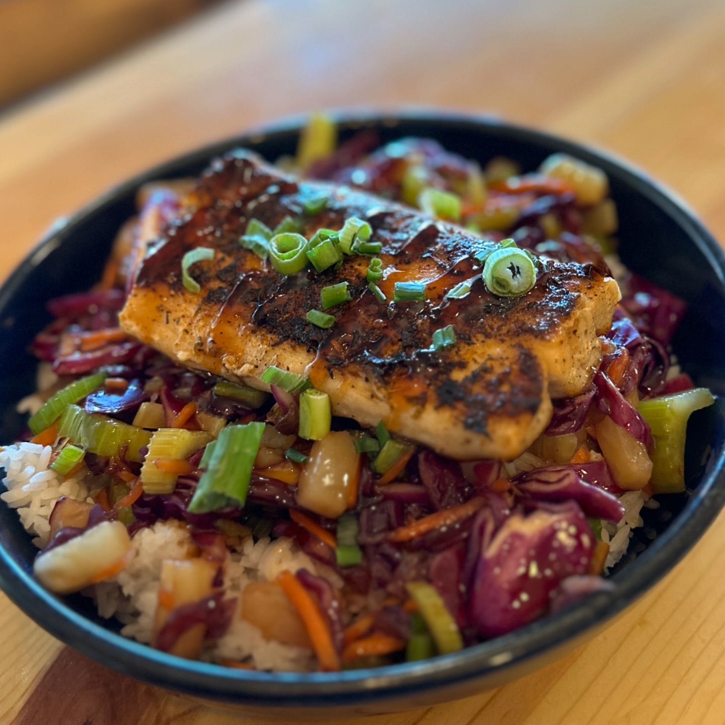Salmon teriyaki bowl with rice and vegetables, garnished with green onions.