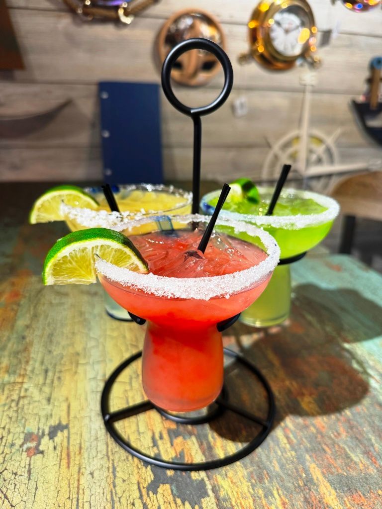 Three margaritas are sitting on a wooden table.
