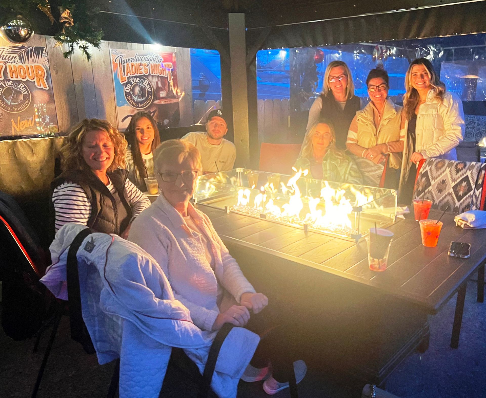A group of people sitting around a table with a fire pit in the background