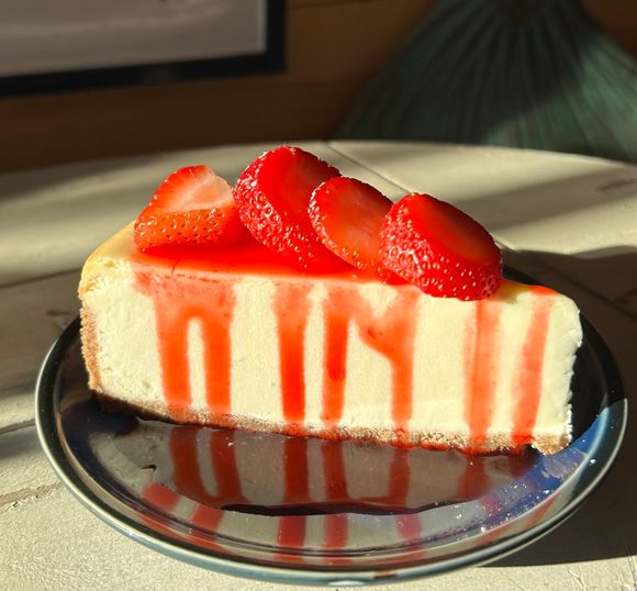 Slice of cheesecake with strawberry topping and red drizzle on a silver plate.