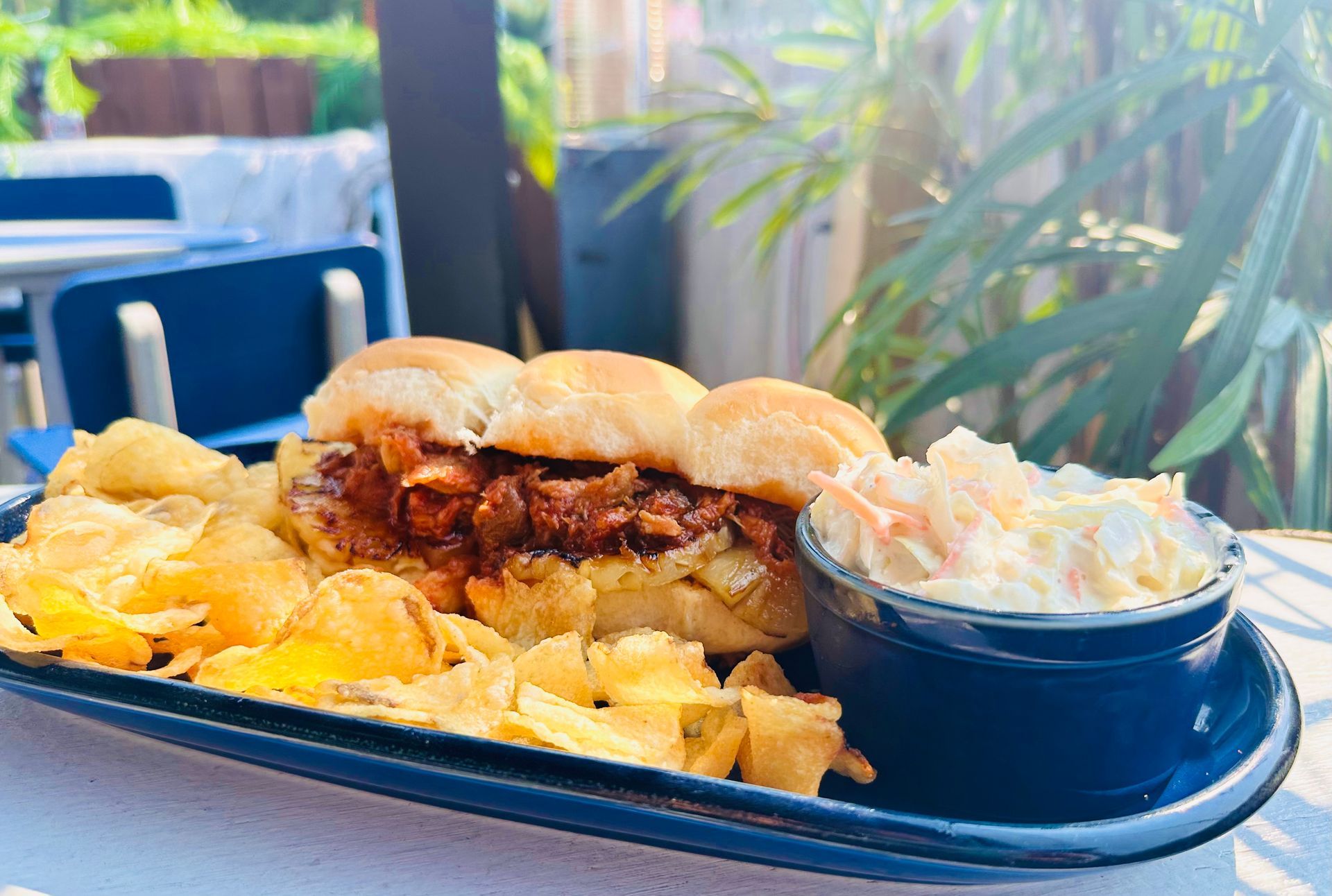Pulled pork sliders, potato chips, and coleslaw on a blue platter outdoors.