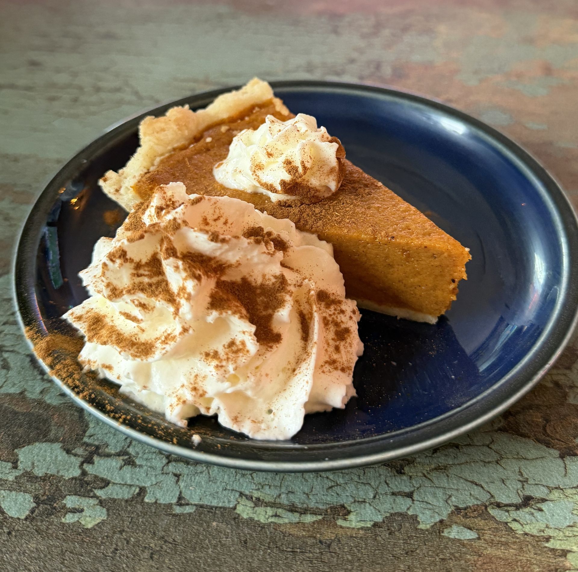 Slice of pumpkin pie with whipped cream and cinnamon on a blue plate.