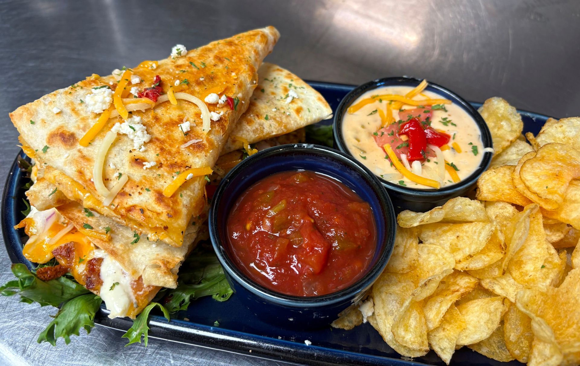 Quesadilla with dips and chips. Cheese quesadilla cut in half next to salsa, cheese dip and chips on a plate.