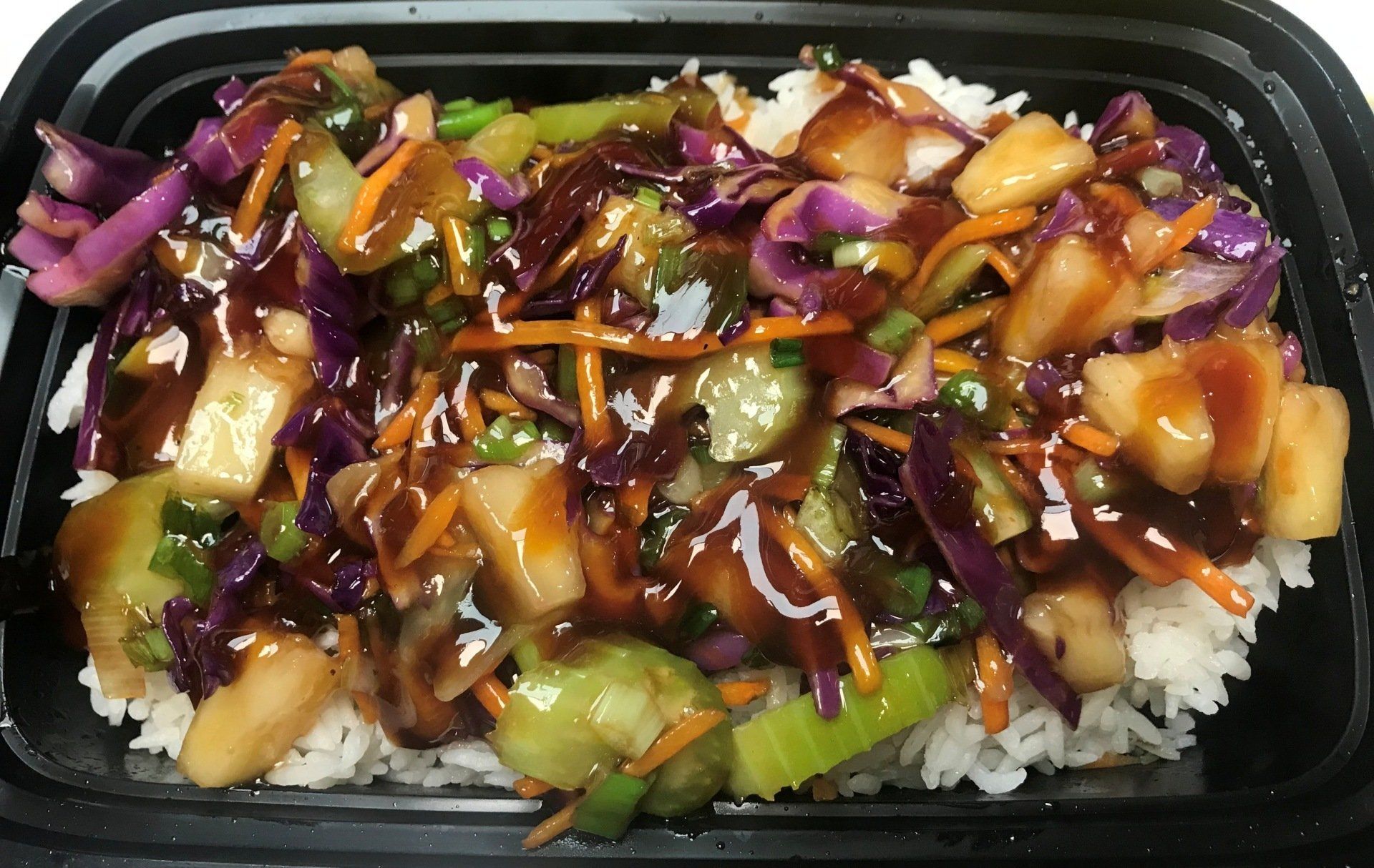 Rice bowl with stir-fry vegetables, pineapple, and sauce in a black container.