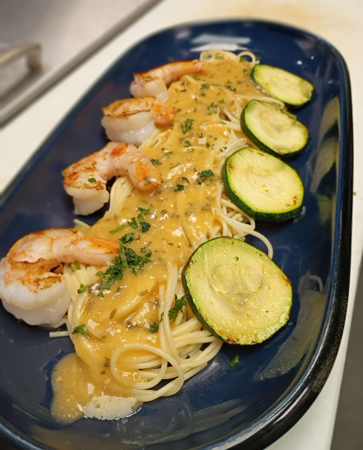 Shrimp scampi pasta with zucchini on a blue plate. Shrimp are seared and sauce is golden.