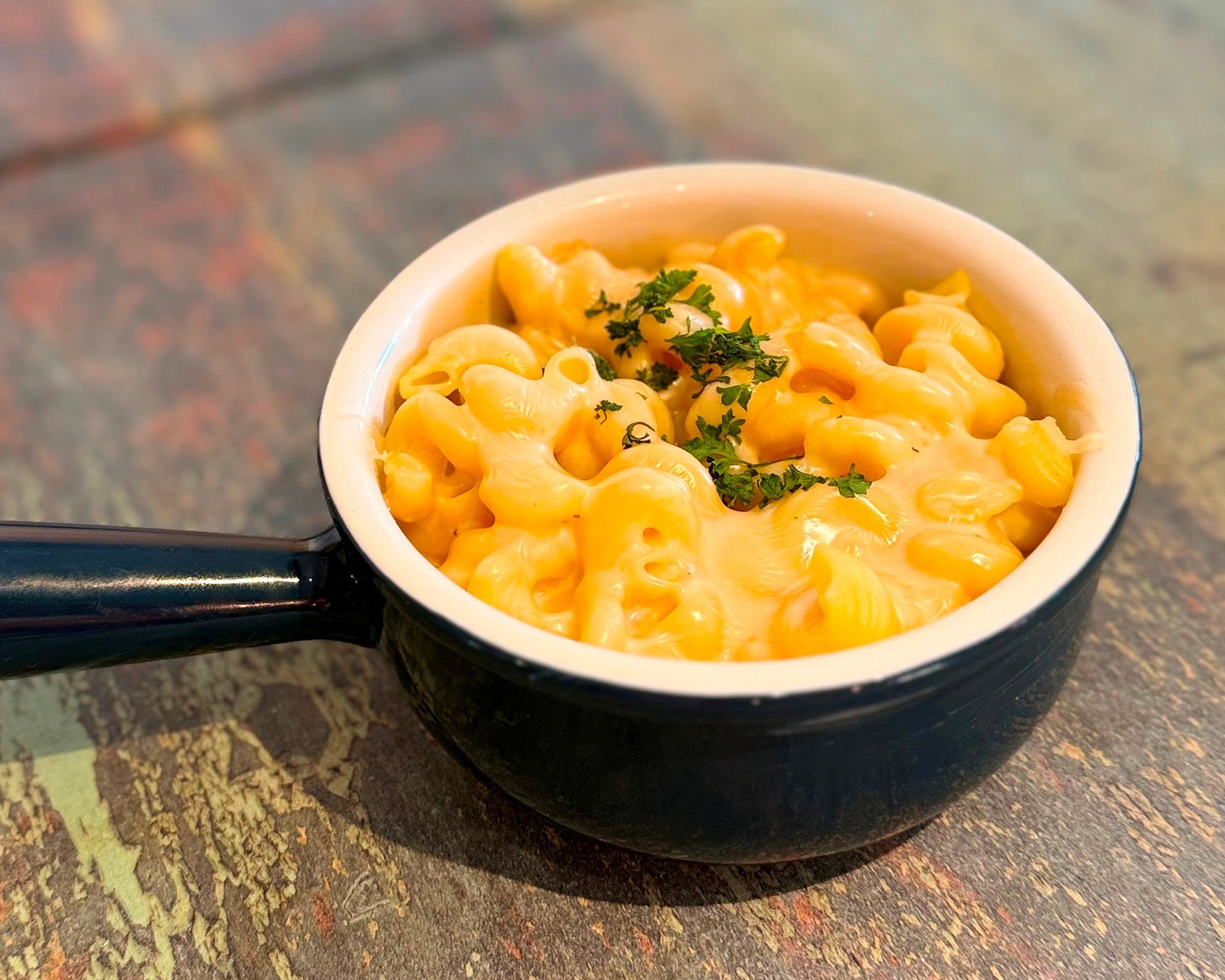 Mac and cheese in a small, black handled bowl on a wooden table.