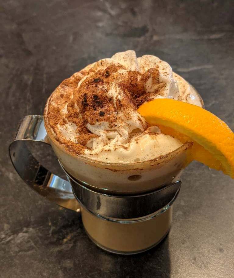 A cup of coffee with whipped cream and an orange slice on top.