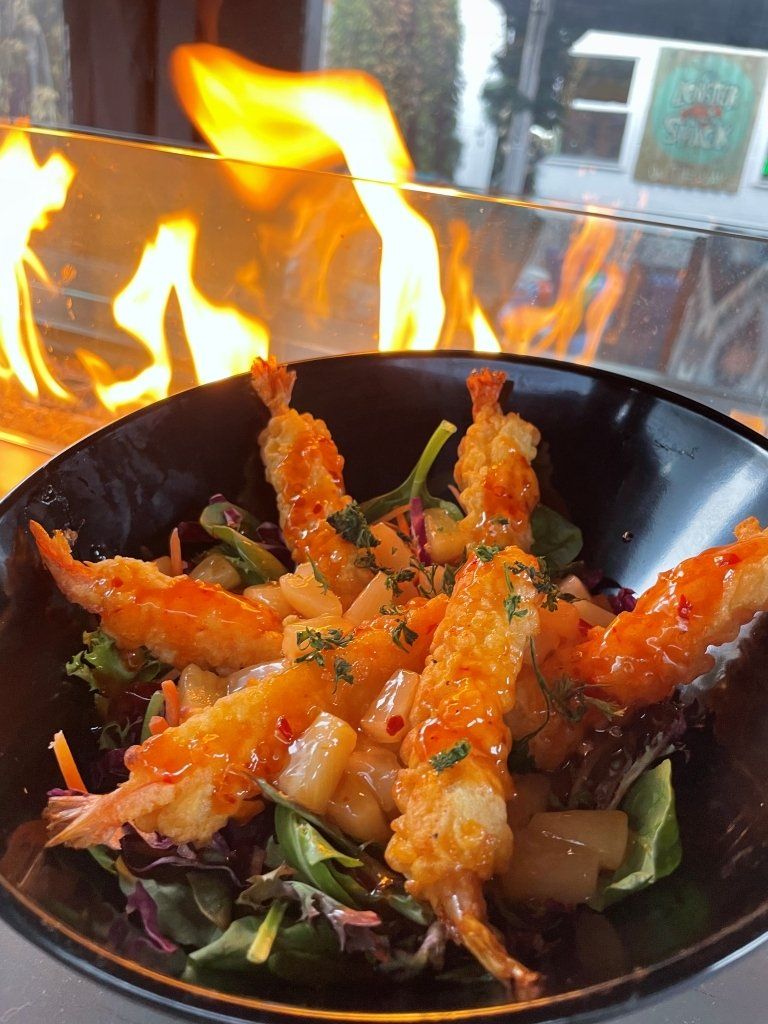 Tempura shrimp salad in a black bowl; flames in the background.
