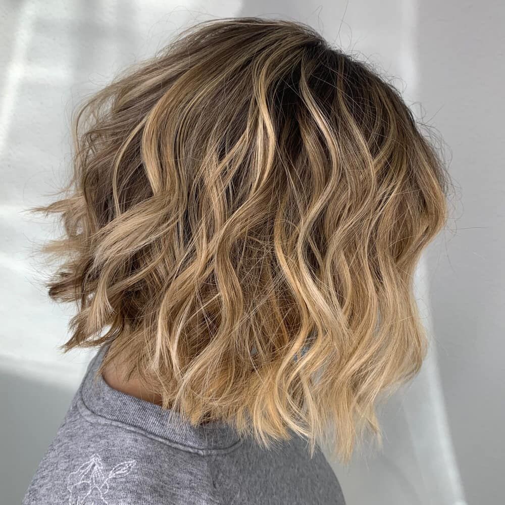 A Woman With Short Wavy Blonde Hair Is Wearing A Grey Sweater — Kabello Salon In Cannonvale, QLD