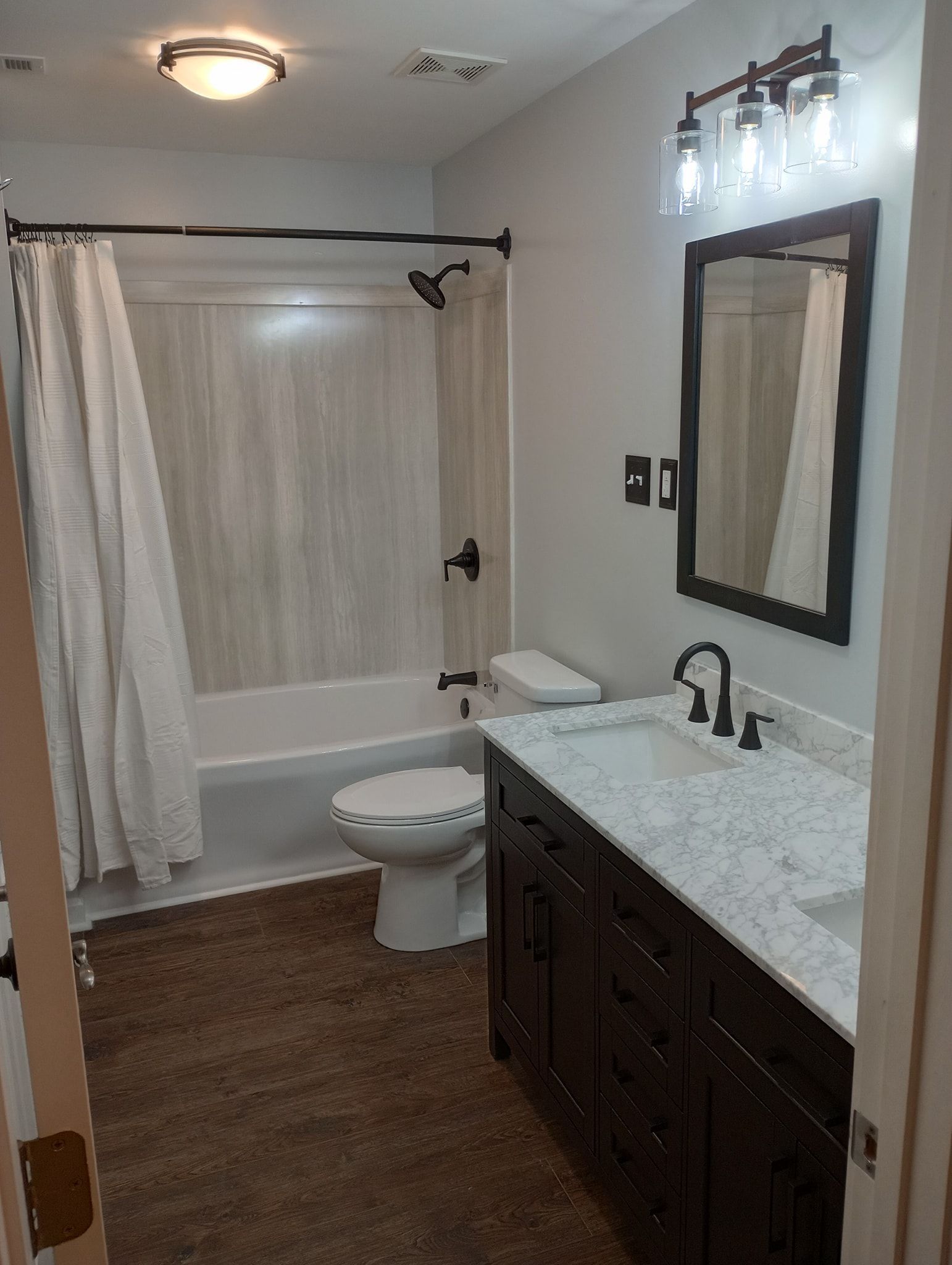 Bathroom with dark wood vanity, white countertop, white toilet, and a bathtub with a shower curtain.