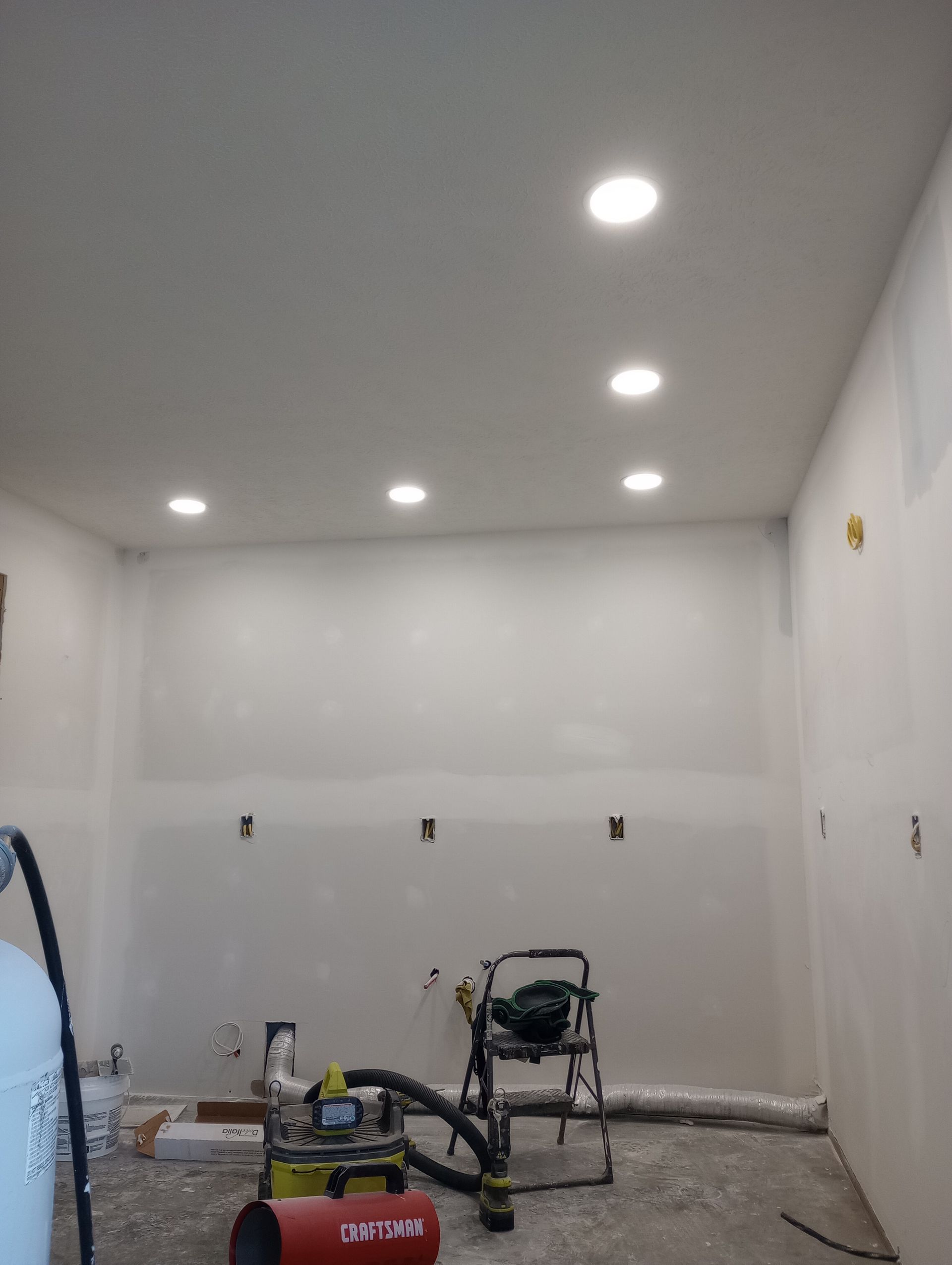 Interior construction in progress, with recessed ceiling lights, bare walls, and tools on the floor.