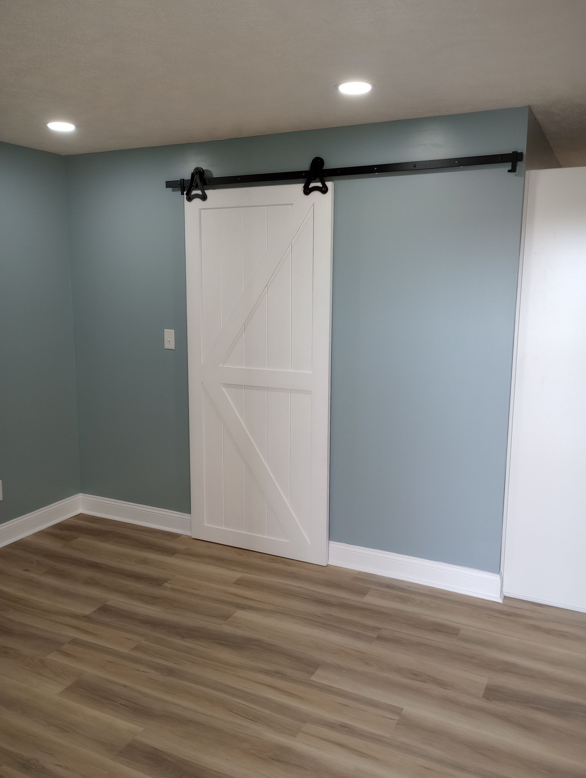 White barn door on blue wall, sliding on black track above wood-look flooring.