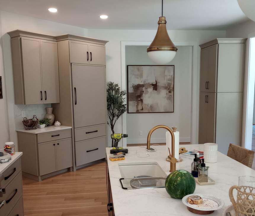 Kitchen with tan cabinets, island with sink, gold faucet, and abstract painting.