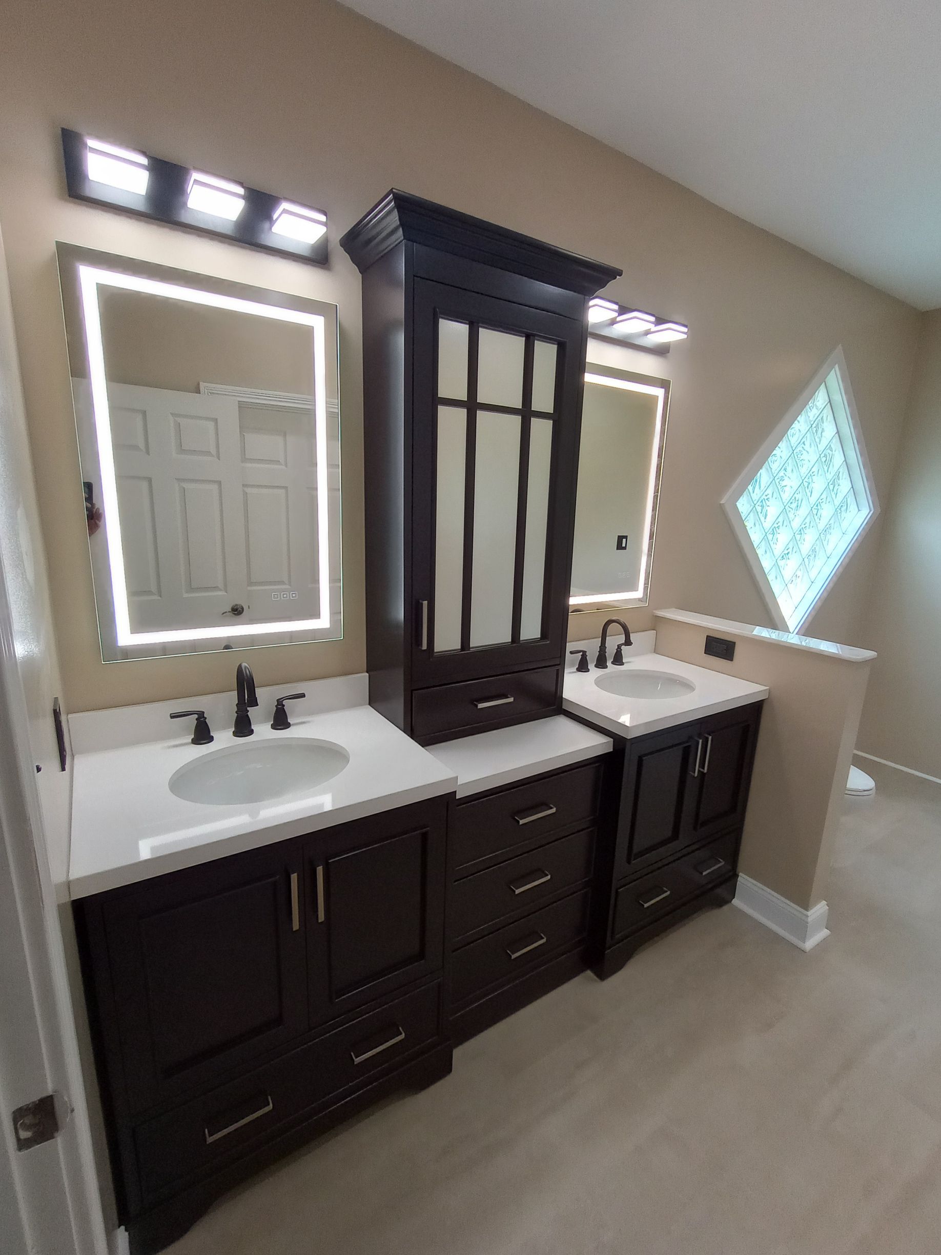 Dark brown bathroom vanity with sinks and mirrors. A dark cabinet sits between.